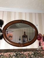 Front view of oval wood framed mirror hung on a striped wallpaper wall, showing the carved square decoration details on the frame and the reflection inside the mirror.