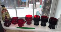 Full lot with red glassware and decorated pottery vase displayed on window ledge.