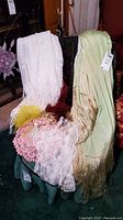 View of three shawls draped over chair, two white crochet doilies and one pink doily on chair seat, button craft angel with yellow feather on chair arm.