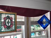 View of both stained glass art pieces hanging in a window, showing size and color contrast with natural light.