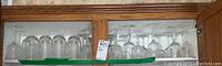 Wooden cabinet shelf containing multiple types of glassware including wine glasses and goblets arranged side by side.