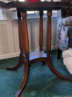 Close-up view of the vintage wooden side table's base showing four large twisted spindle legs and curved feet with some scratches and scuffs.