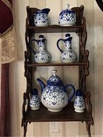 Frontal photo of the teapot, salt and pepper shakers, oil and vinegar cruets, creamer and sugar bowl arranged on the decorative wooden wall shelf.