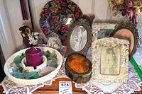 Various Victorian-style framed prints, sea glass in white ceramic bowl with candle, small oval trinket box, and decorative wire boot displayed on lace tablecloth.