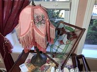 Victorian style lamp with pink fringed shade next to stained glass suncatcher on a table
