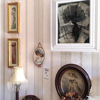 View of framed Victorian ladies wall art on striped wallpaper with white lamp and floral decoration under oval frame