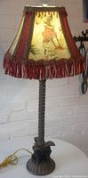 Full frontal view of lamp showing figural monkey base, leafy stem, and original painted monkey-themed shade with fringe.