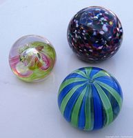 Top view of three colorful glass paperweights showing ribbon, spotted, and striped designs.