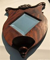 Top-down angled view of shield-shaped oak mirror with bevelled diamond mirror, carved wooden detail at top, and built-in small rounded shelf at bottom.