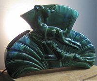 Side view of green glazed fan-shaped ceramic lamp with raised figural animals.
