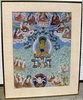 Front view of framed Buddhist oil painting showing central Buddha with multiple surrounding figures and decorative flora, framed with a linen mat.