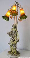 Full view of the art glass lily lamp with figurine base showing three illuminated lily-shaped shades and sculpted woman and child figures.