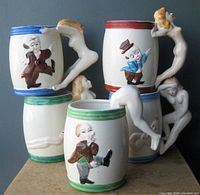 Full view of stacked ceramic coffee mugs showing nude lady-shaped handles and cartoon character illustrations on the sides
