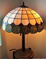 Photograph showing the lamp lit indoors with detailed view of the multicolored stained glass dome shade and base.