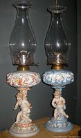 Front view of both porcelain cherub hurricane oil lamps side by side