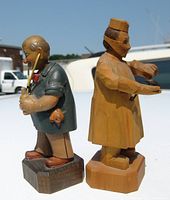 Side and front views of two carved wood medical professional sculptures displayed outdoors on a white surface.