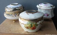 Photo shows three Nippon Noritake porcelain vanity boxes with lids, displaying floral and gold hand-painted decoration in Art Nouveau style.