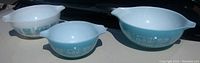 Three Pyrex Amish Farmer Butterprint mixing bowls arranged by size showing turquoise and white patterns on sides and interiors.