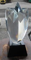 Front view of clear heavy glass abstract shooting star sculpture on black base showing facets and overall shape.