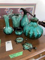 Seven Blue Mountain Pottery pieces: urn with lid, two vases, bowl, jug with handle and two turtle figurines with a green and black drip glaze finish on a wooden surface