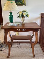 Front view of wooden table with green lamp, floral arrangement, and dresser set pieces on top.