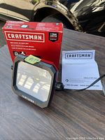 Photo of the Craftsman LED work light, showing the light, power cord, and instruction manual on a wooden surface.