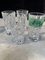 Four clear Ralph Lauren shot glasses upright on a surface with a green sticker on one glass