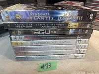 Stack of eight Stargate DVDs including Stargate Atlantis, Stargate SG-1, Stargate Universe with DVD spines showing titles mainly in French language for Stargate Atlantis and SG-1 series. Five remain sealed.