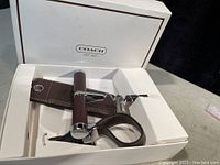 Open white Coach branded box showing corkscrew with leather handle and bottle stopper attached to leather loop handle.