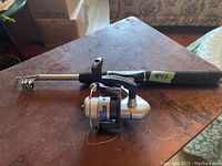 Photo of folding telescopic fishing pole with Shimano reel on a wooden table, showing the entire pole folded with the reel attached.