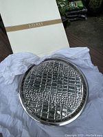 Photo of circular metal bar tray with crocodile pattern, still in packaging with tissue paper and original box visible.
