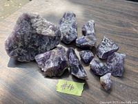 Ten pieces of amethyst rocks laid out on a table, showing natural rough purple crystals and formation textures.
