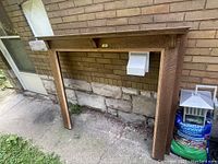 Front view showing the full antique oak fireplace mantle placed outdoors against a brick and stone wall to give size perspective.