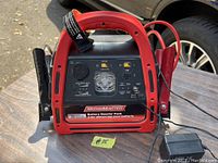 Front view of red MotoMaster battery booster pack with clamp cables, control panel, USB port, LED light, and labels visible.