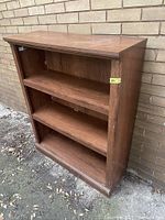 Front and side angle photo showing wooden bookshelf with three shelves, highlighting its structure and wear.