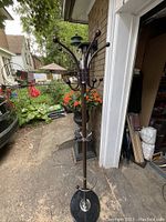 Full view of the metal coat tree standing outside near a garage, showing height and structure with hooks spaced at multiple levels.