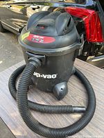 Black Shop-Vac wet/dry vacuum cleaner on a table outdoors front and side view showing hose and vacuum body with brand and specification labels