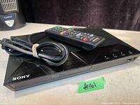 Sony Blu-ray DVD player with remote control on top and power cable beside it.