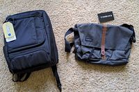 Photo shows both bags side by side on a carpeted floor, tags visible on both indicating new condition.