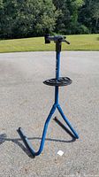 Full view of the blue Park Tool PCS-1 bike repair stand showing foldable legs and accessory tray on a driveway outdoors.