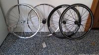 Four bicycle wheels leaning against a wall on carpeted floor