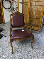 Front angled view of maroon leather armchair showing carved wood frame and brass nailhead trim.