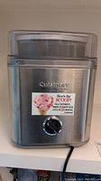 Front view of stainless steel Cuisinart ice cream maker with clear lid and dial control on front.