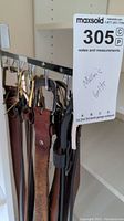 Photo of various men's belts hanging on hooks showing different leather colors and metal buckles