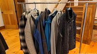 Wide view of seven men's jackets and coats hanging on rack, in various colors including black, grey, and blue.