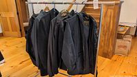 Photo showing multiple men's jackets and coats hanging on a rack indoors; primarily dark colored outerwear.