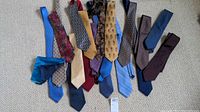 Array of assorted neckties laid out on beige carpet, showing various colors including blue, red, gold, black, and patterned designs.
