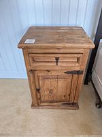 Front view of single pine nightstand showing drawer and door with metal hardware and natural finish.
