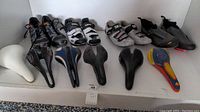 Full lot view showing cycling shoes and bike saddles arranged in a single row on a white surface