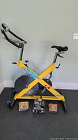 Yellow LeMond RevMaster Classic indoor cycle with DVD cases and pedal box on floor